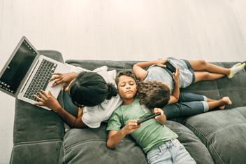 Mother using laptop while her two children using smartphones.