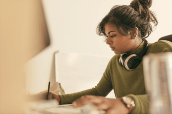 Woman works at desktop and takes notes.