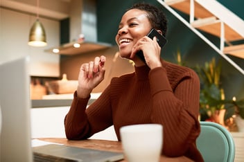 Woman speaking on phone in front of her laptop at home
