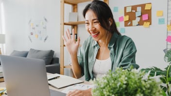 Woman smiling and waving in virtual interview on laptop