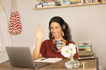 Woman waving to laptop screen in virtual meeting