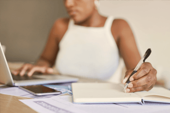 Woman working at laptop taking notes in notebook