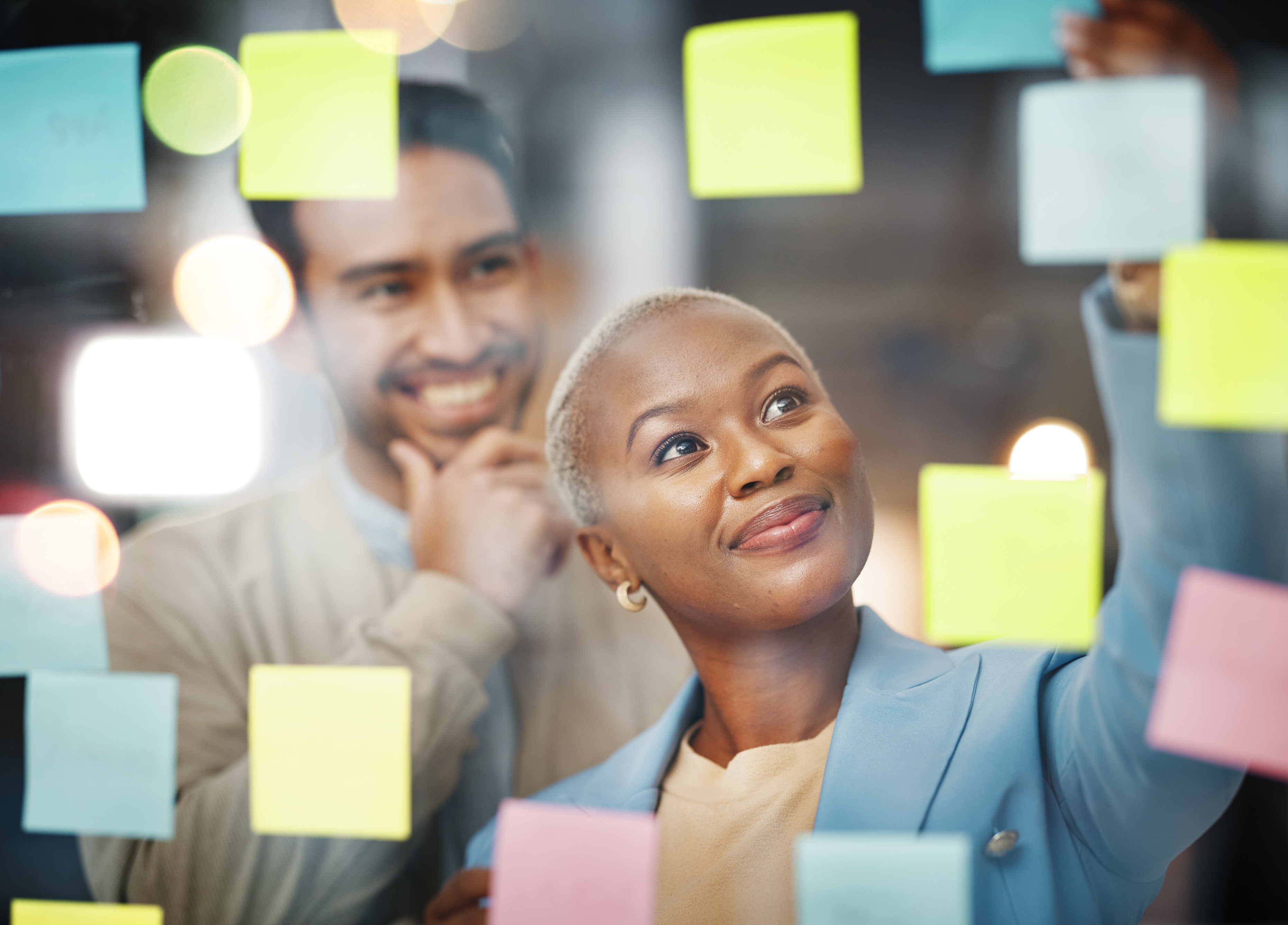 African American women looking at glass wall of post it notes